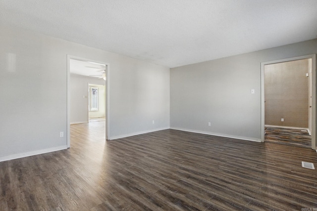 empty room featuring a textured ceiling, dark wood-style flooring, and baseboards