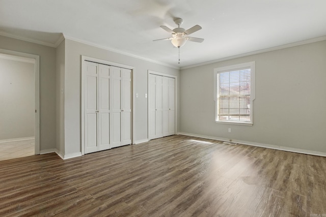 unfurnished bedroom featuring crown molding, multiple closets, a ceiling fan, wood finished floors, and baseboards