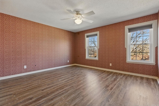 empty room featuring a textured ceiling, dark wood-type flooring, baseboards, and wallpapered walls