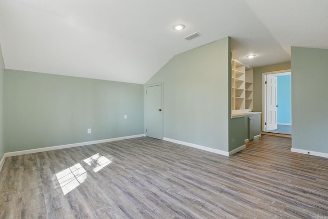 additional living space with lofted ceiling, visible vents, baseboards, and wood finished floors