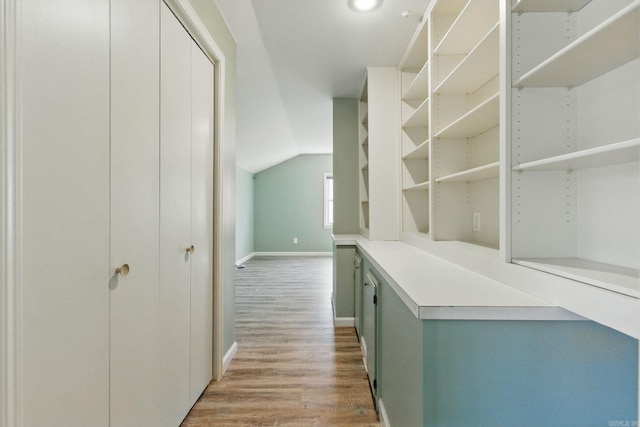 corridor with light wood-style floors, baseboards, and vaulted ceiling