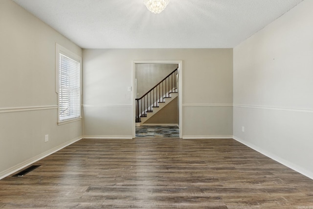 spare room featuring visible vents, stairway, a textured ceiling, wood finished floors, and baseboards