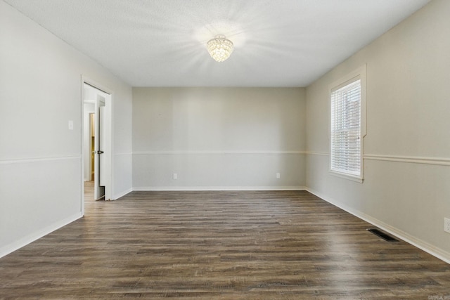 empty room with baseboards, visible vents, and dark wood-style flooring