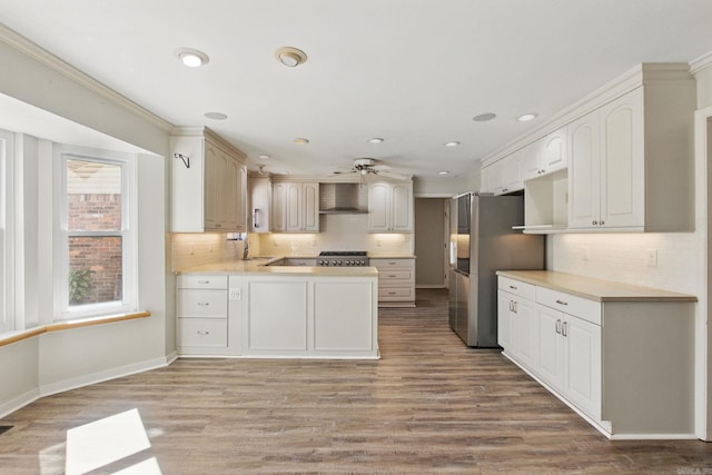 kitchen featuring stove, freestanding refrigerator, wood finished floors, a peninsula, and wall chimney exhaust hood