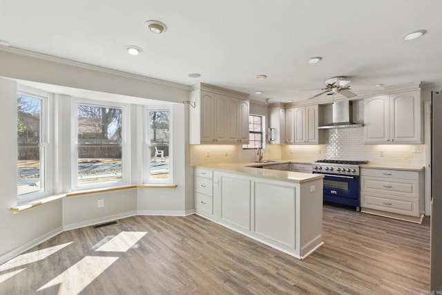 kitchen featuring light wood-style flooring, light countertops, high end stainless steel range oven, and wall chimney range hood