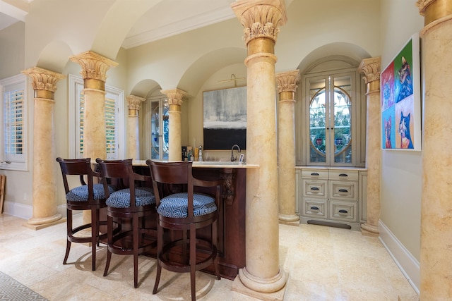 bar featuring ornate columns, baseboards, and crown molding