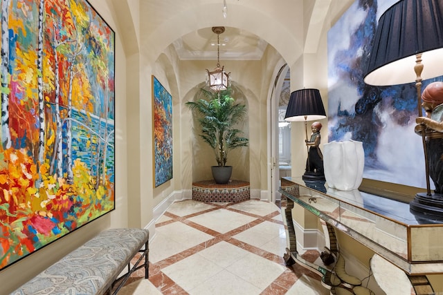 corridor featuring arched walkways, baseboards, a raised ceiling, and crown molding