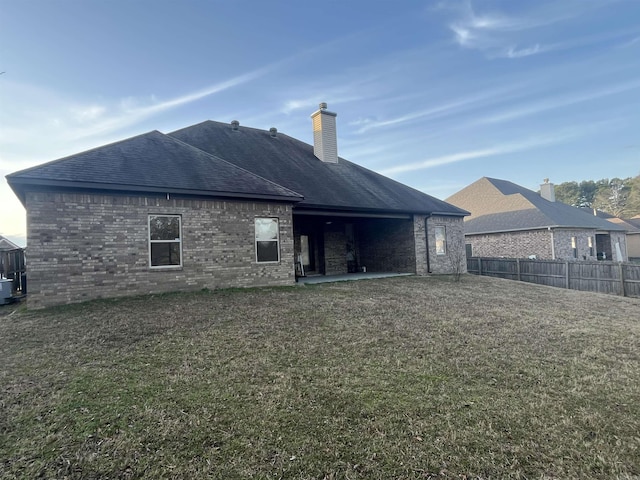 back of property featuring brick siding, fence, and a lawn