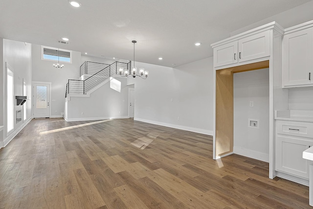 unfurnished living room featuring a chandelier, wood finished floors, visible vents, and stairs