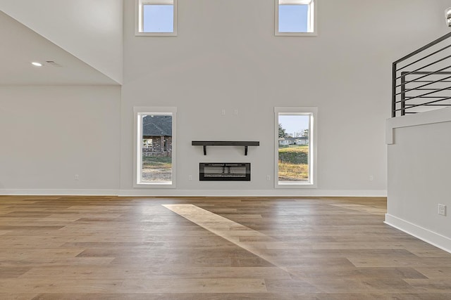 unfurnished living room with wood finished floors, a glass covered fireplace, a high ceiling, and baseboards