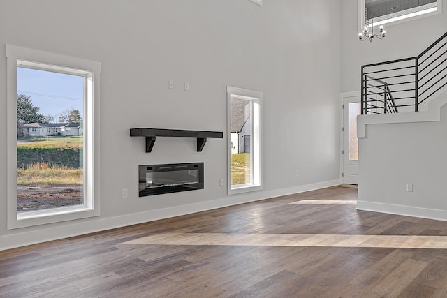 unfurnished living room featuring a notable chandelier, heating unit, wood finished floors, baseboards, and stairs