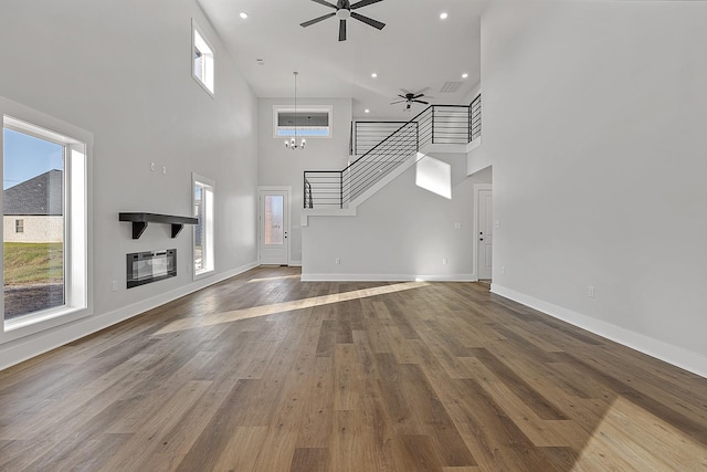 unfurnished living room featuring stairs, heating unit, wood finished floors, baseboards, and ceiling fan with notable chandelier