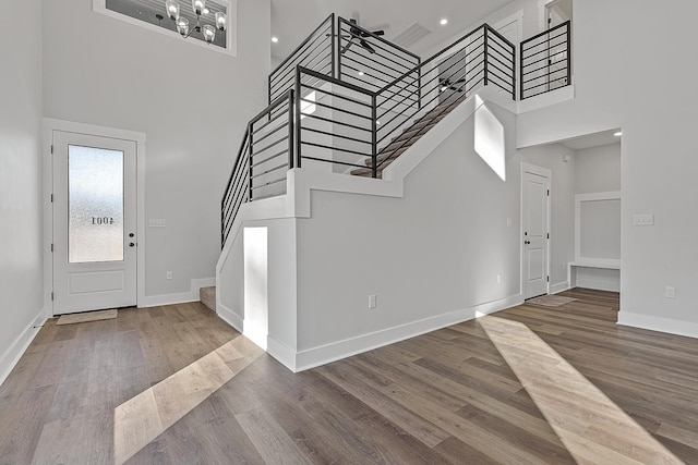 entryway with stairway, wood finished floors, and a towering ceiling