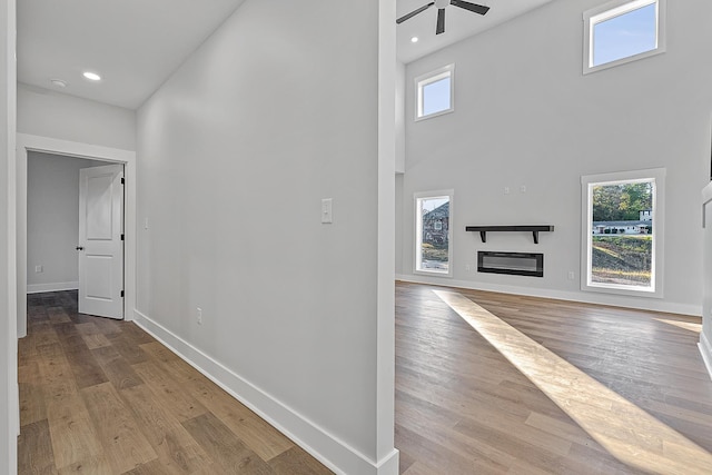 corridor featuring baseboards, wood finished floors, heating unit, a high ceiling, and recessed lighting