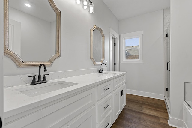 full bathroom with double vanity, a sink, baseboards, and wood finished floors