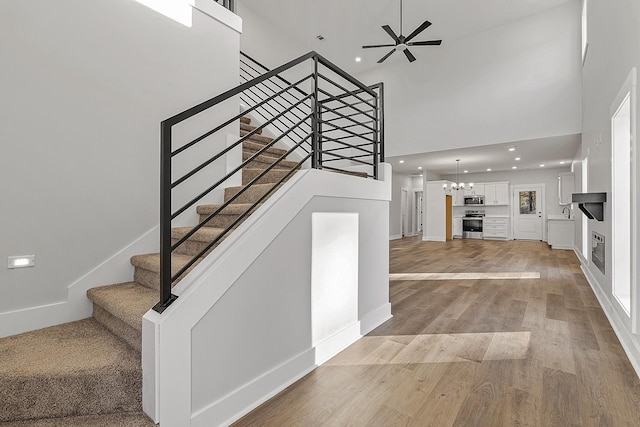 stairway featuring recessed lighting, a towering ceiling, wood finished floors, a tile fireplace, and ceiling fan with notable chandelier