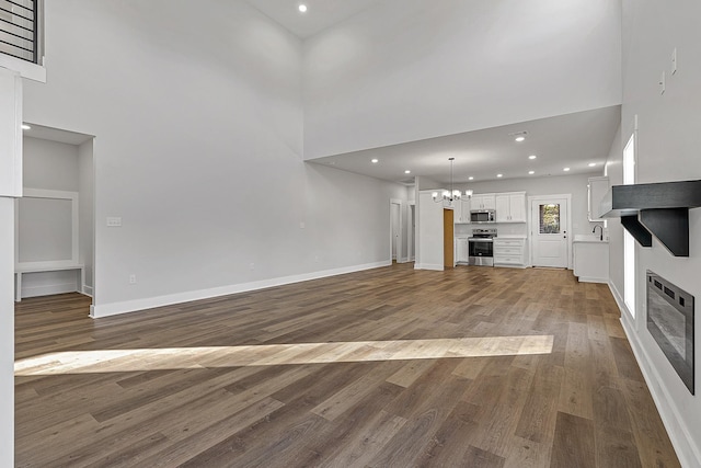 unfurnished living room with a chandelier, a high ceiling, dark wood-style flooring, baseboards, and a glass covered fireplace