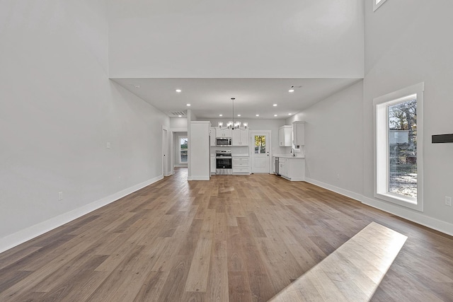 unfurnished living room with light wood-type flooring, baseboards, a notable chandelier, and recessed lighting