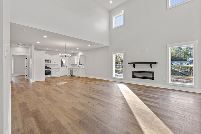 unfurnished living room featuring a chandelier, baseboards, a glass covered fireplace, and light wood-style floors