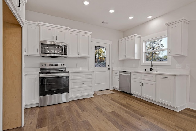 kitchen featuring visible vents, wood finished floors, stainless steel appliances, light countertops, and a sink