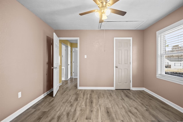 unfurnished bedroom featuring attic access, baseboards, ceiling fan, and wood finished floors