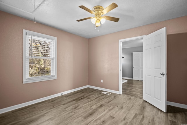 spare room with visible vents, attic access, ceiling fan, wood finished floors, and baseboards