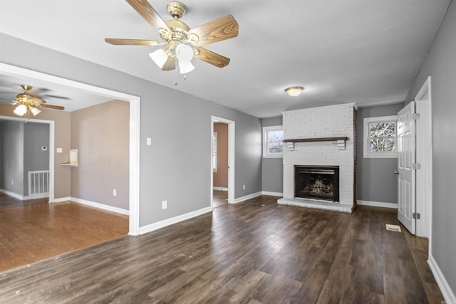 unfurnished living room featuring a brick fireplace, visible vents, a wealth of natural light, and wood finished floors