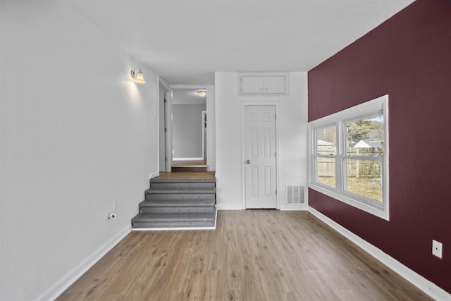 empty room featuring stairs, visible vents, baseboards, and wood finished floors