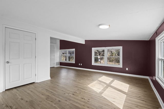 unfurnished room featuring a wealth of natural light, lofted ceiling, baseboards, and wood finished floors