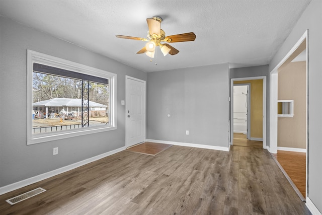 empty room with baseboards, a textured ceiling, visible vents, and wood finished floors