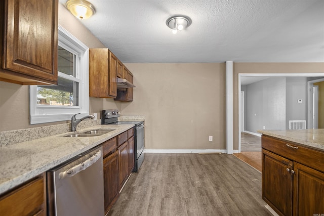 kitchen featuring under cabinet range hood, a sink, appliances with stainless steel finishes, light stone countertops, and dark wood-style floors