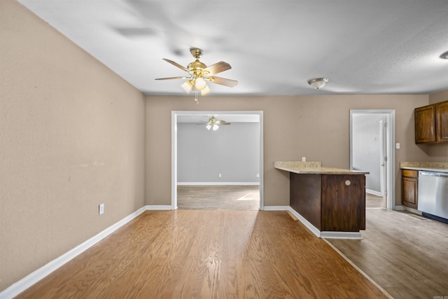 kitchen featuring a peninsula, wood finished floors, baseboards, light countertops, and stainless steel dishwasher