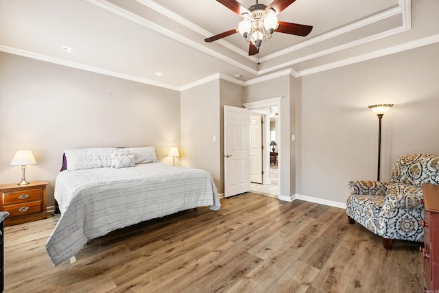 bedroom featuring baseboards, wood finished floors, a raised ceiling, and crown molding