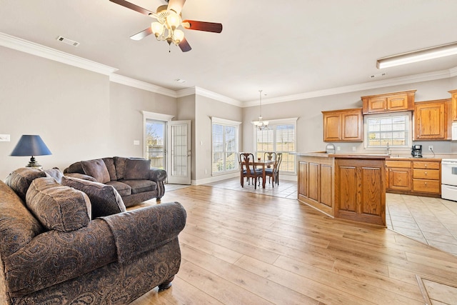 living room with light wood-style flooring, ceiling fan with notable chandelier, visible vents, baseboards, and crown molding