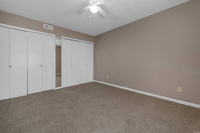 unfurnished bedroom featuring carpet flooring, a ceiling fan, baseboards, visible vents, and multiple closets