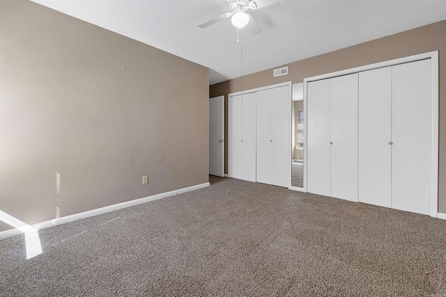 unfurnished bedroom featuring visible vents, ceiling fan, a textured ceiling, carpet floors, and two closets