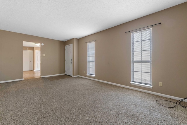 spare room with baseboards, a textured ceiling, and light colored carpet