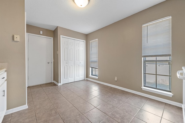 unfurnished bedroom with a closet, a textured ceiling, baseboards, and light tile patterned floors