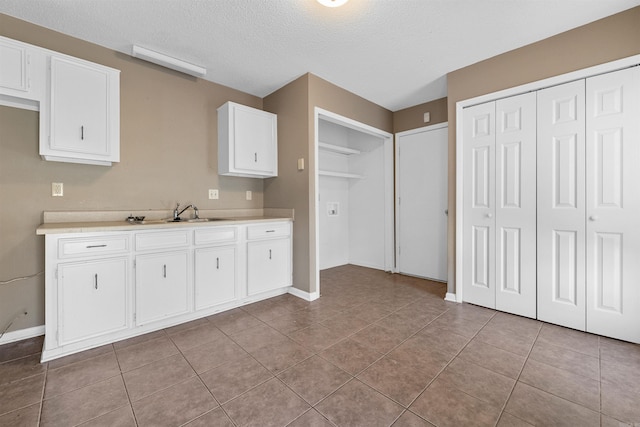 kitchen with light tile patterned floors, light countertops, white cabinets, a sink, and a textured ceiling