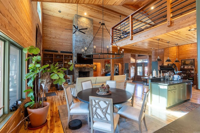 dining space with wooden walls, high vaulted ceiling, wood finished floors, and a stone fireplace