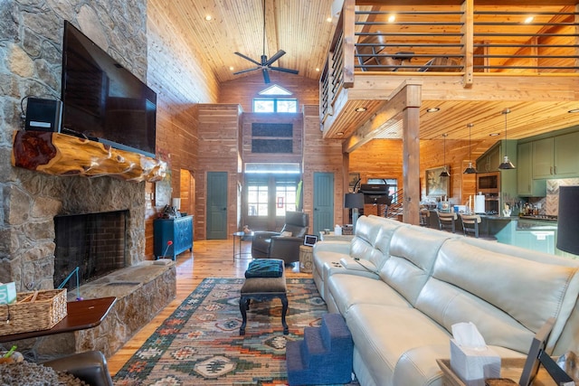 living room featuring wooden ceiling, light wood-style flooring, a stone fireplace, wood walls, and high vaulted ceiling