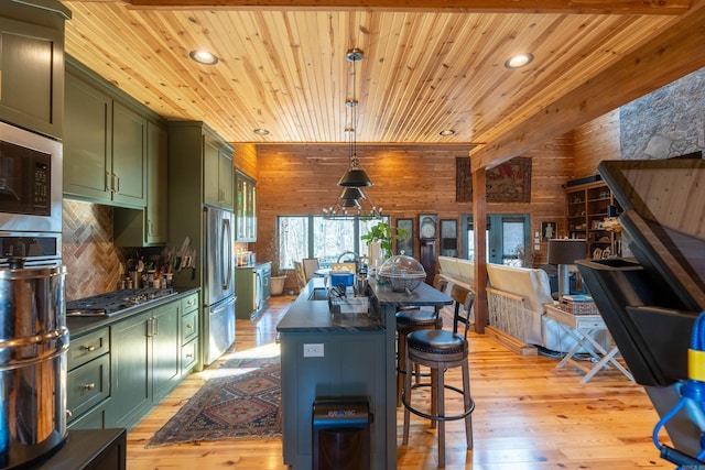 kitchen with wooden walls, stainless steel appliances, green cabinets, light wood-type flooring, and dark countertops