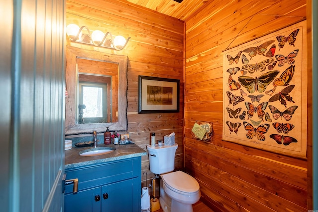 half bath with toilet, wooden walls, and vanity