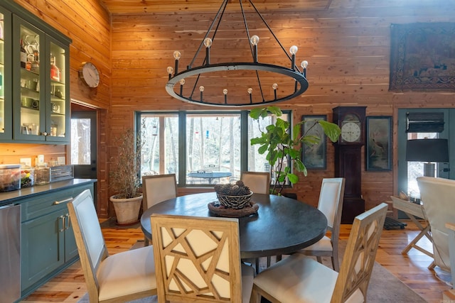 dining room featuring a towering ceiling, light wood finished floors, wooden walls, and a notable chandelier