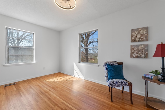 sitting room with baseboards, a textured ceiling, visible vents, and wood finished floors