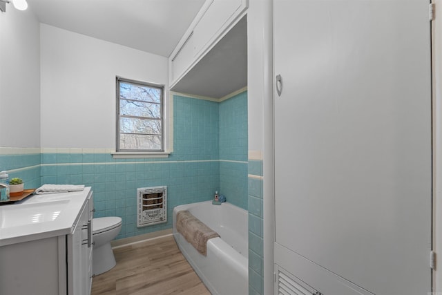 full bath with a garden tub, wood finished floors, vanity, tile walls, and heating unit