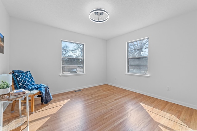 sitting room with plenty of natural light, visible vents, baseboards, and wood finished floors