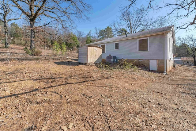 rear view of house with an outbuilding, crawl space, central AC, and a storage shed