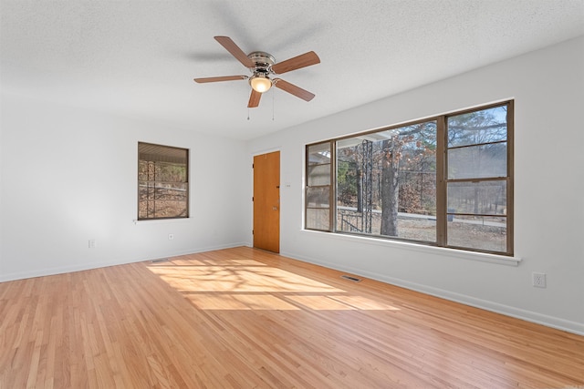 unfurnished room with a textured ceiling, wood finished floors, a ceiling fan, visible vents, and baseboards