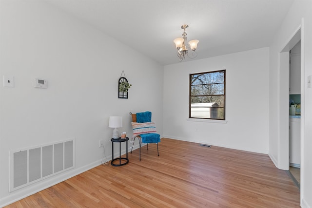 sitting room with a chandelier, light wood-type flooring, visible vents, and baseboards